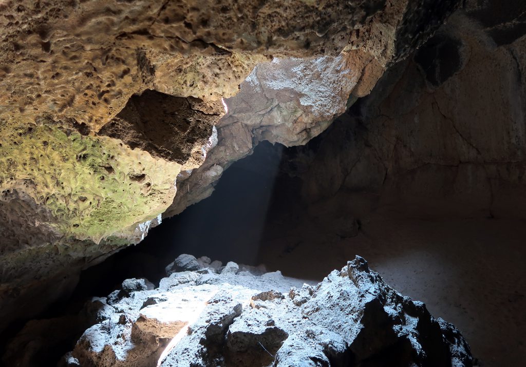 A bean of sunlight breaches into the moist, misty landscape of a lava tube cave at Lava Beds National Monument.